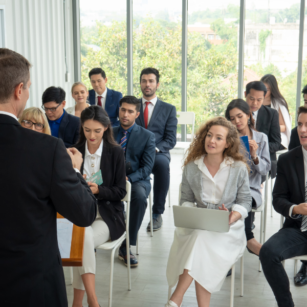 Professional seminar or workshop with attendees in formal attire listening to a speaker, suitable for corporate training or leadership events.