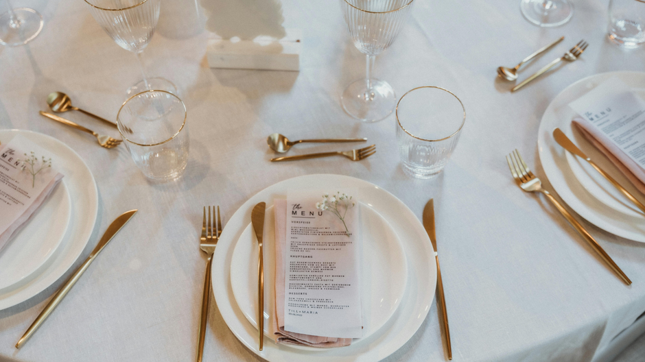 disposable party tableware with white plates and golden cutlery on a tabel with white tablecloth 