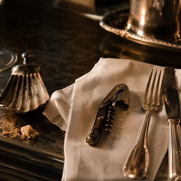 Fine dining server tools including crumber, wine key, and polished flatware on a formal table