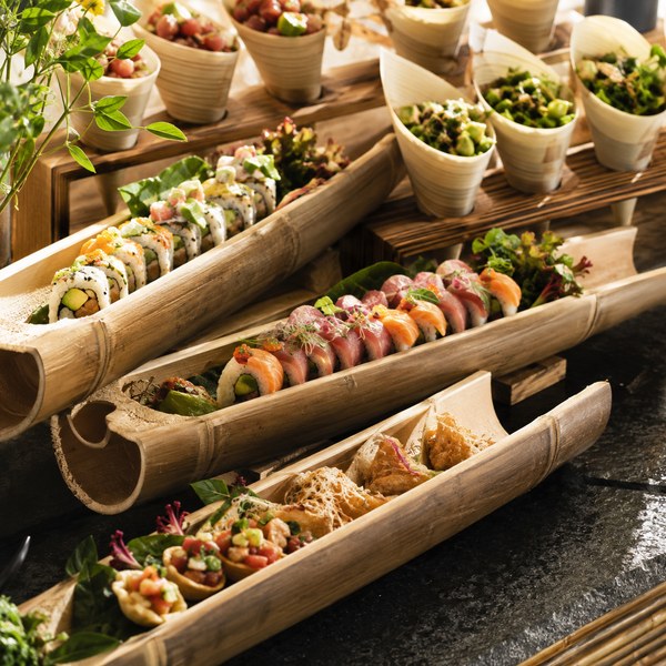 Bamboo canoe serving boats displaying sushi and appetizers beside bamboo food cones on a buffet