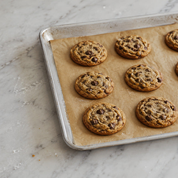 Chocolate chip cookies baking evenly on a light-colored aluminum half-sheet pan lined with parchment paper