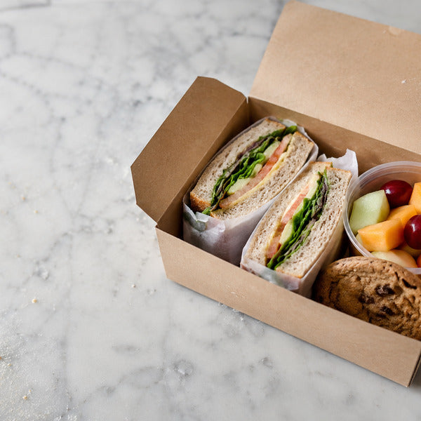 Boxed picnic lunch with sandwich, fruit cup, and cookie for a catered company picnic