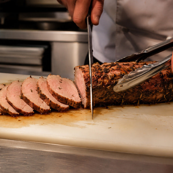 Carving knife slicing roasted pork tenderloin, one of the leanest pork cuts, at a foodservice station