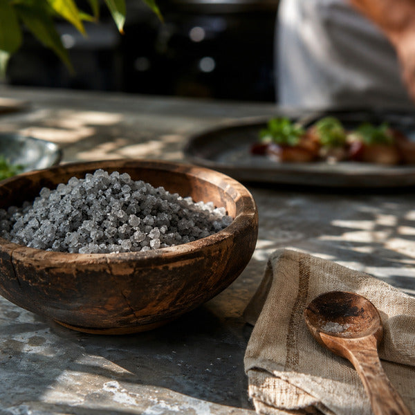 Coarse gray celtic sea salt crystals in a wooden bowl on a chef's prep station