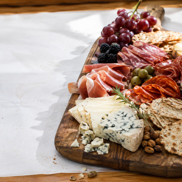 Rustic charcuterie board with prosciutto, salami, blue cheese, brie, grapes, blackberries, olives, and crackers on a wood serving board