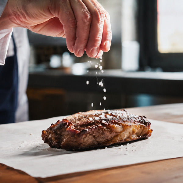 Chef finishing a seared steak with a pinch of celtic sea salt at the pass