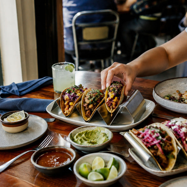 Taco bar setup for cinco de mayo foods with tacos served upright in stainless steel taco holders