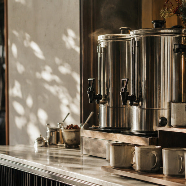Commercial coffee station setup with stainless urns, tiered risers, and ceramic mugs for holiday service