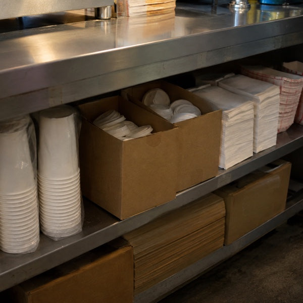 Concession stand supplies of cups, lids and napkins held as par stock on a shelf above the floor.