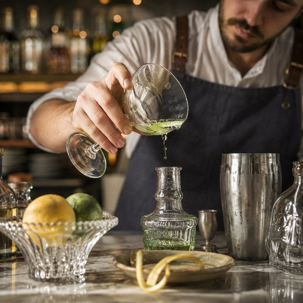 Bartender rinsing a coupe with absinthe while making a corpse reviver cocktail recipe