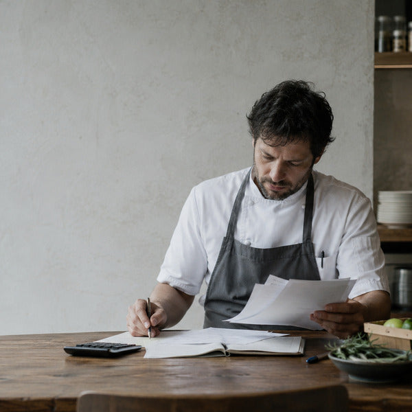 Chef reviewing invoices and inventory to cut food purchase costs in a restaurant kitchen