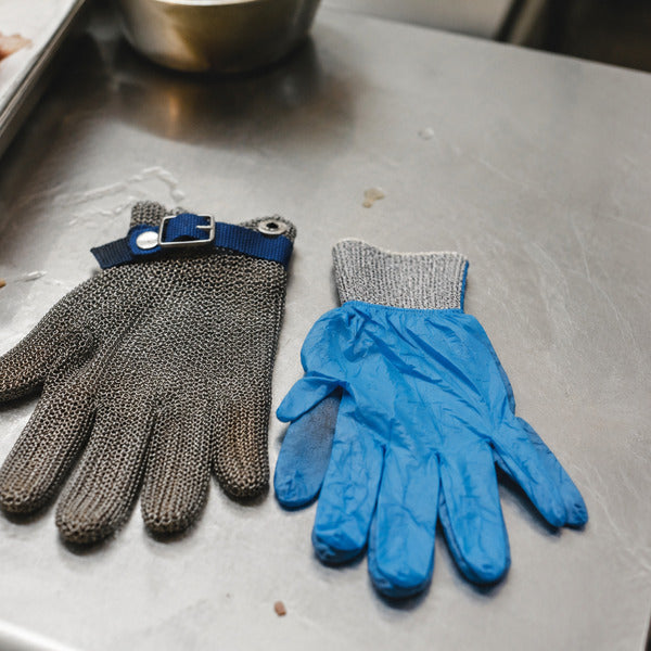 Stainless steel mesh cut resistant glove next to a knit cut resistant glove layered under a food-safe disposable nitrile glove