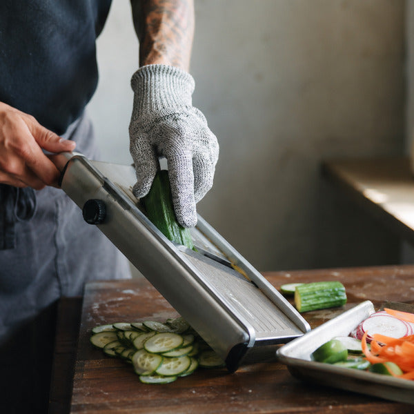 Prep cook wearing a level 5 cut resistant glove while slicing vegetables on a mandoline