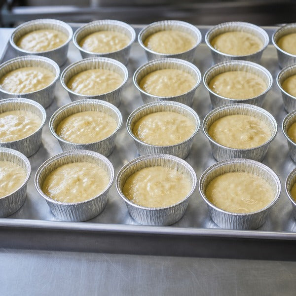 Freestanding foil baking cups filled with muffin batter arranged on a sheet pan without a muffin tin