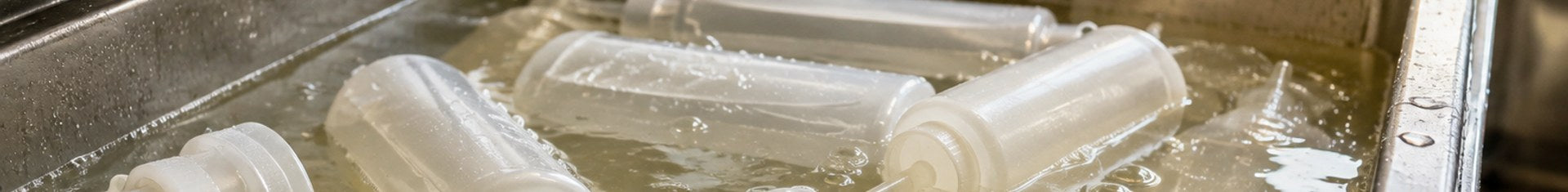 Squeeze bottles soaking in food safe sanitizer solution in a three-compartment commercial sink