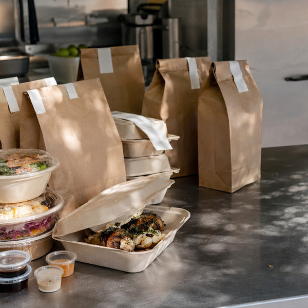 Ghost kitchen packing station with take-out containers, tamper-evident bags, and labeled delivery orders