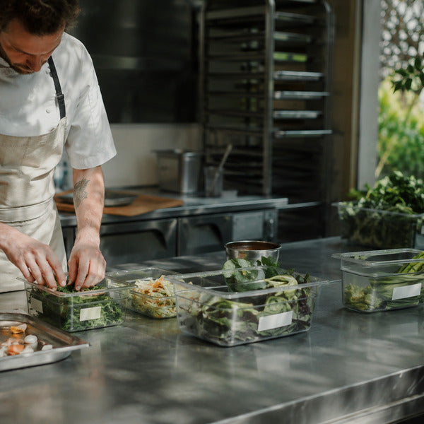 Chef learning how to reduce food waste at a commercial kitchen prep station with labeled containers