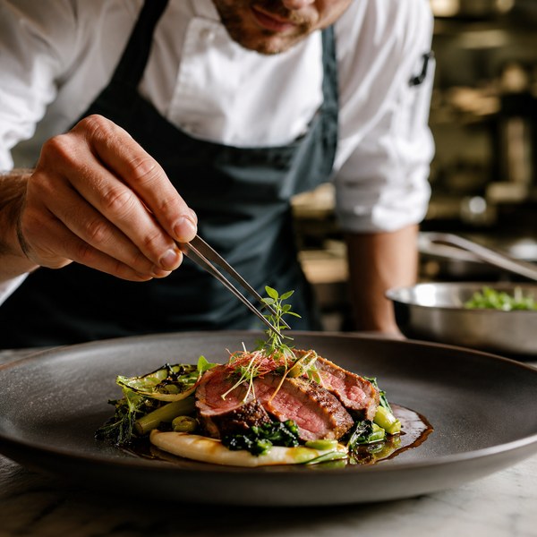Chef using plating tools to finish a photogenic dish for an influencer marketing shoot in a restaurant kitchen