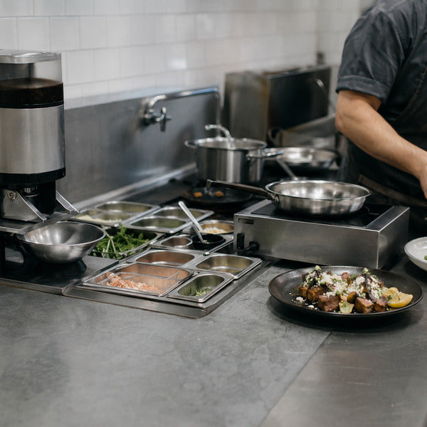 Chef plating on a stainless prep line with organized hot wells and saute pans