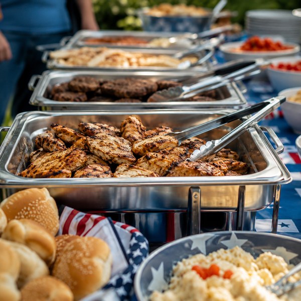 Buffet table with serving trays and chafing dishes portioned for a Memorial Day cookout crowd