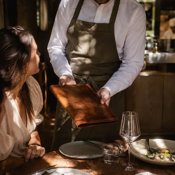Server presenting a leather-bound menu to guests, showing menu presentation in a full-service dining room
