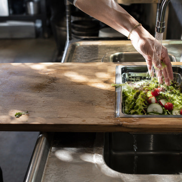 Adjustable over-the-sink cutting board with collapsible strainer on a commercial kitchen sink