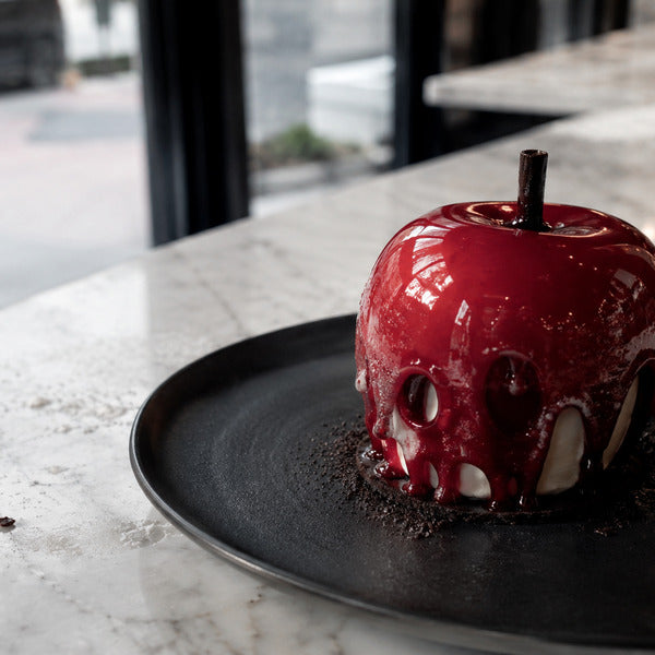 Poison apple panna cotta Halloween dessert with red mirror glaze on a black plate