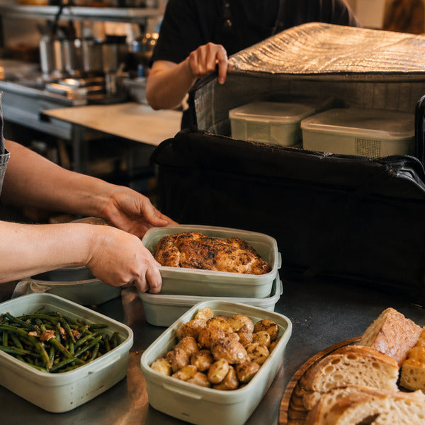 Kitchen staff packing family meal deals into vented to-go containers and an insulated delivery bag