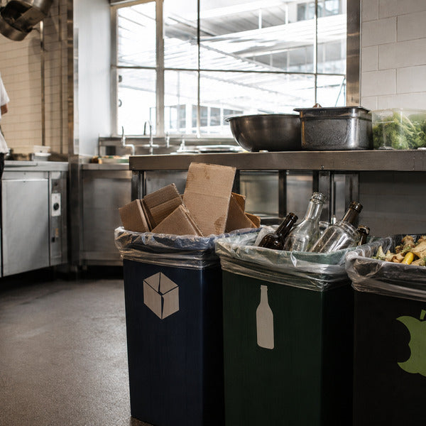 Restaurant recycling station with labeled bins for cardboard, glass, and organics in a commercial kitchen