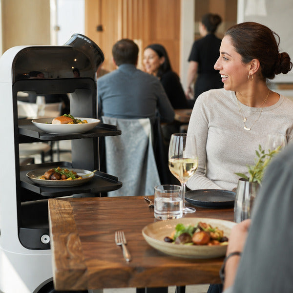 Food service robot serving plated meals to guests in a restaurant dining room.