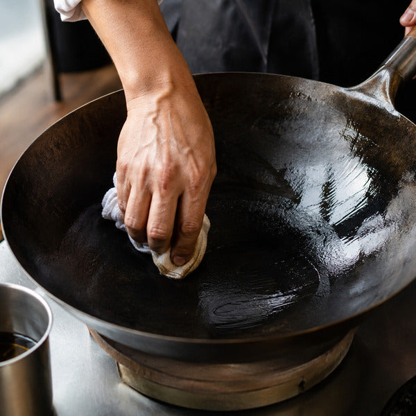 Cook wiping oil into a hot carbon steel wok to build a dark nonstick seasoning patina