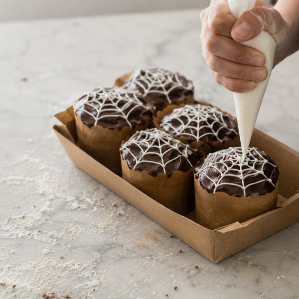 Piping a spiderweb pattern on chocolate Halloween cupcakes