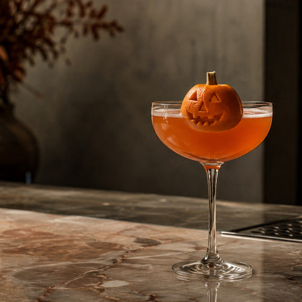Halloween jack-o-lantern cocktail in a coupe glass with carved orange peel garnish