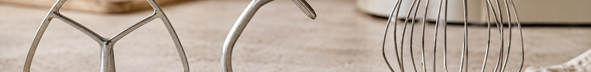 Stand mixer attachments laid out on a prep counter: flat beater, dough hook, and wire whisk