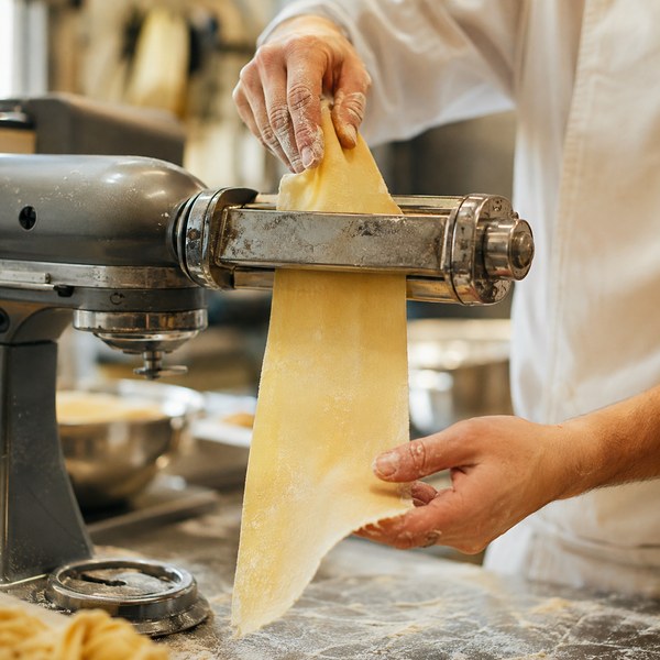 Chef feeding dough through a pasta roller, one of the most-used stand mixer attachments in commercial kitchens