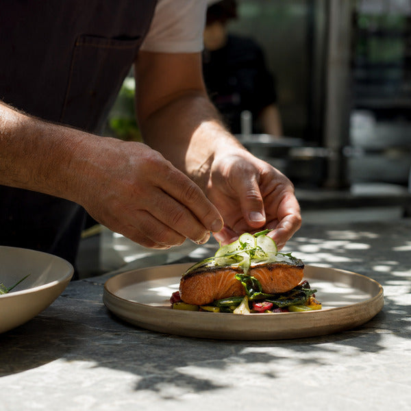 Chef plating sustainable seafood entree with certified wild-caught salmon in a restaurant kitchen