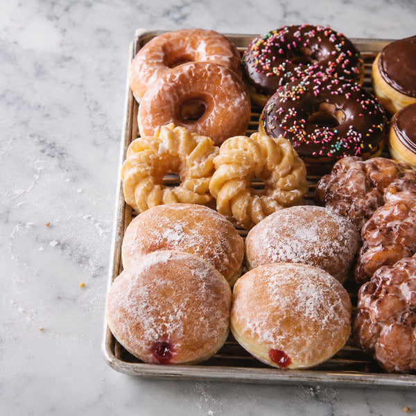 Assortment showing many types of donuts including glazed, frosted, jelly-filled, crullers, and fritters on a bakery display tray